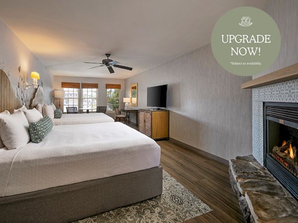 A cozy hotel room with two beds, a fireplace, seating area, flat-screen TV, and a warm, inviting decor. End.