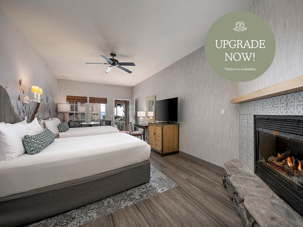 A cozy hotel room with a large bed, fireplace, flat-screen TV, and seating area in warm, calming tones.