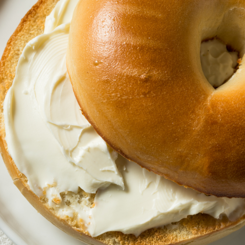 A bagel with cream cheese on a plate, photographed from above, showing a golden-brown toasted bagel half with generous white cream cheese.