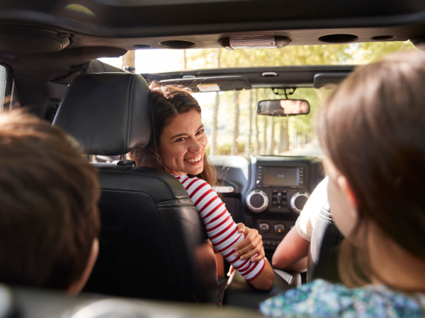 A group of friends in a car, smiling at each other in the back seat during a sunny drive.