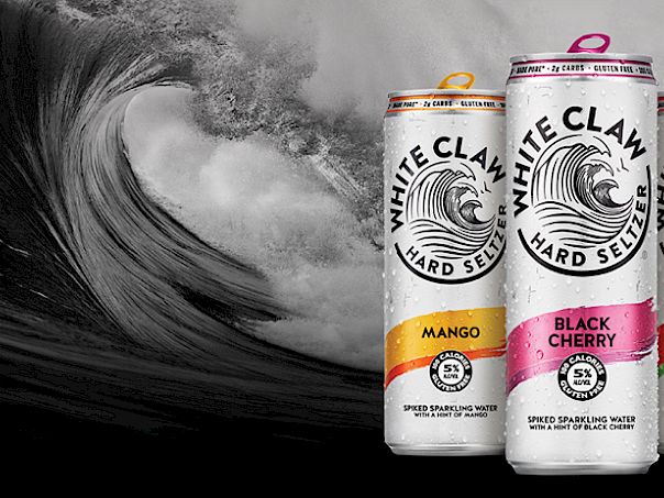 Three cans of White Claw hard seltzer (Mango, Black Cherry, Watermelon) beside a big ocean wave.
