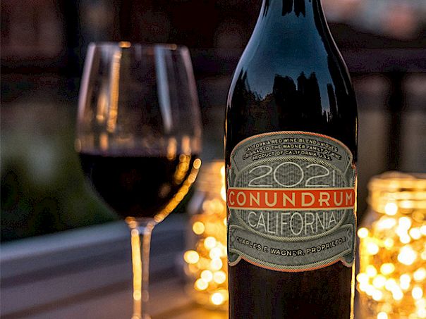A bottle of wine labeled &ldquo;Conundrum&rdquo; with a glass of red wine and candles glowing softly in the background.
