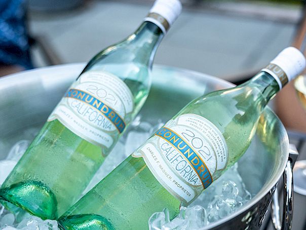Two green glass bottles of mineral water chilling in an ice bucket, with a person holding a wine glass in the background.