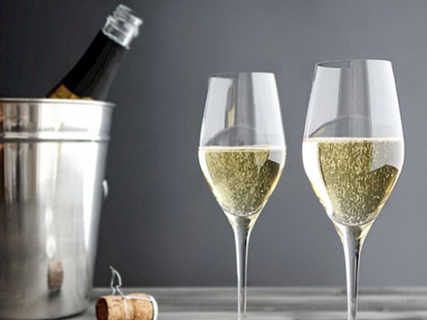 Two champagne flutes filled with sparkling wine sit beside an ice bucket holding a bottle; a cork rests nearby, all against a dark background.