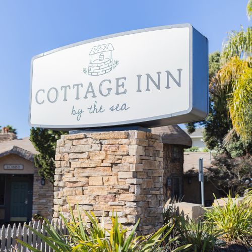A roadside scene with a blue-and-white sign for a hospital or clinic, palm trees, and a small building in the background, sunny day.