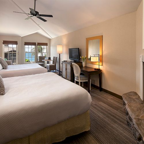 A cozy bedroom with a large bed, soft lighting, a desk and chair, a fireplace, and warm decor.