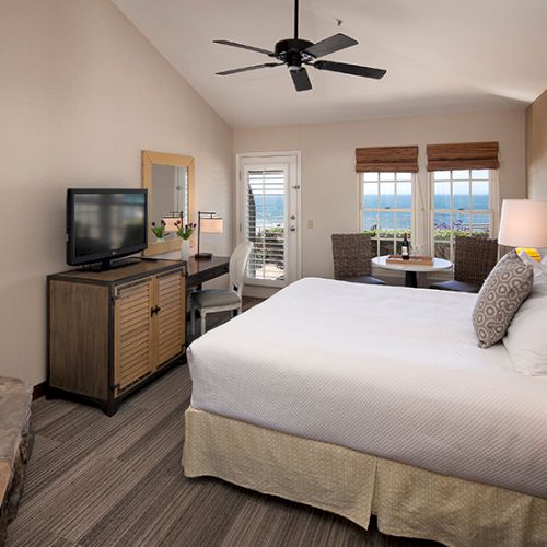 A modern hotel room with two queen beds, hardwood floors, wall art, a work desk, a flat-screen TV, and warm lighting.