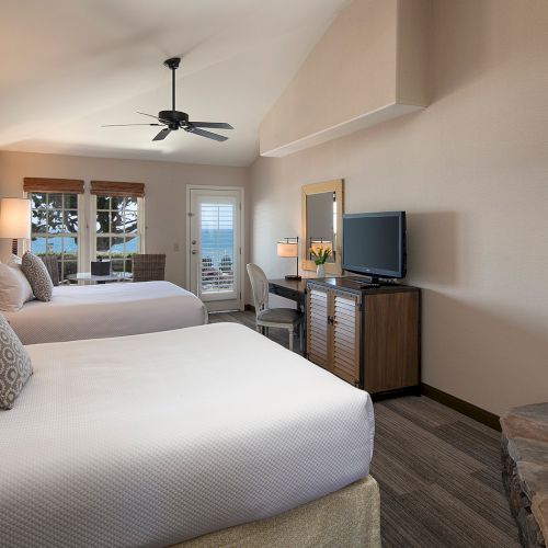 A modern hotel room with a cozy bed, nightstands, a desk, and a seating area, plus soft lighting and neutral decor.