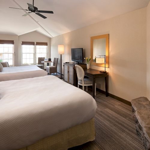 Cozy hotel room with a plush bed, warm lighting, a laptop on a desk, framed art, and a fireplace in the corner, inviting and tidy.