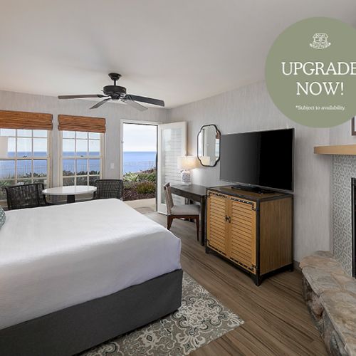 A modern hotel room with a large bed, sofa, desk, flat-screen TV, and a colorful fireplace feature; windows overlook a cityscape.