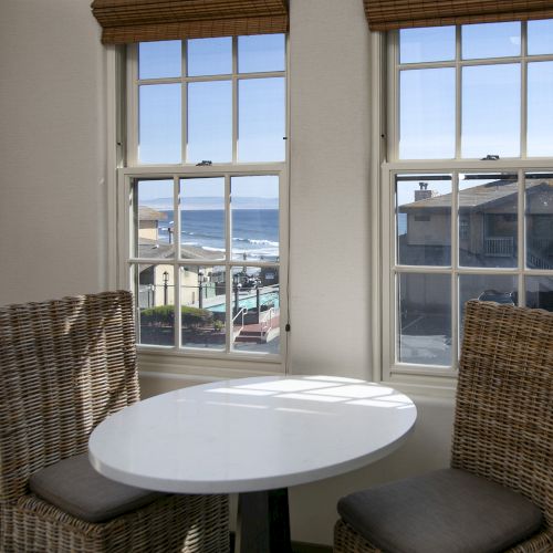 A cozy corner with a round white table between two wicker chairs, large windows offering a cityscape view, natural light flooding the room.