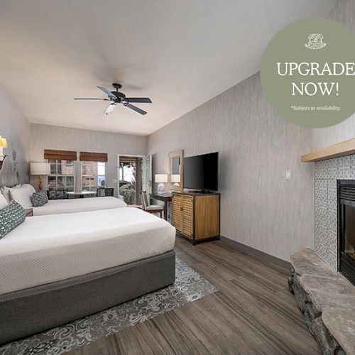 A modern hotel room with a large bed, warm lighting, a fireplace, and a couch in a neutral palette.