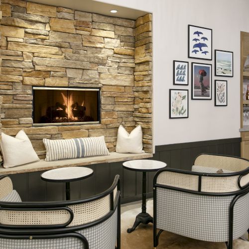Cozy lounge with a stone fireplace, modern chairs, round white tables, and a gallery wall of framed art.