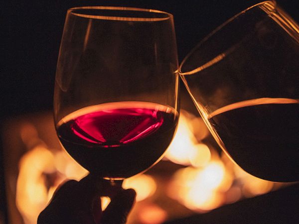 Two clinking wine glasses with red wine, warm glow in the background, celebrating a toast.