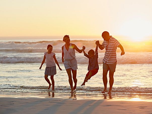 A family of four runs along the beach at sunset, holding hands and laughing as the waves roll in.